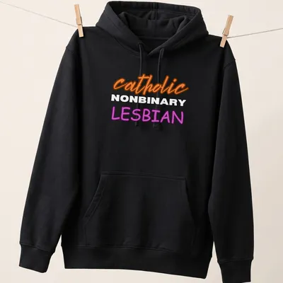 Bold typography design featuring 'catholic NONBINARY LESBIAN' in orange, white, and purple — printed on a unisex hoodie