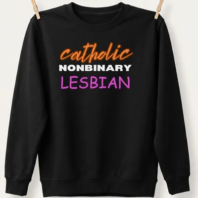 Bold typography design featuring 'catholic NONBINARY LESBIAN' in orange, white, and purple — printed on a unisex sweatshirt