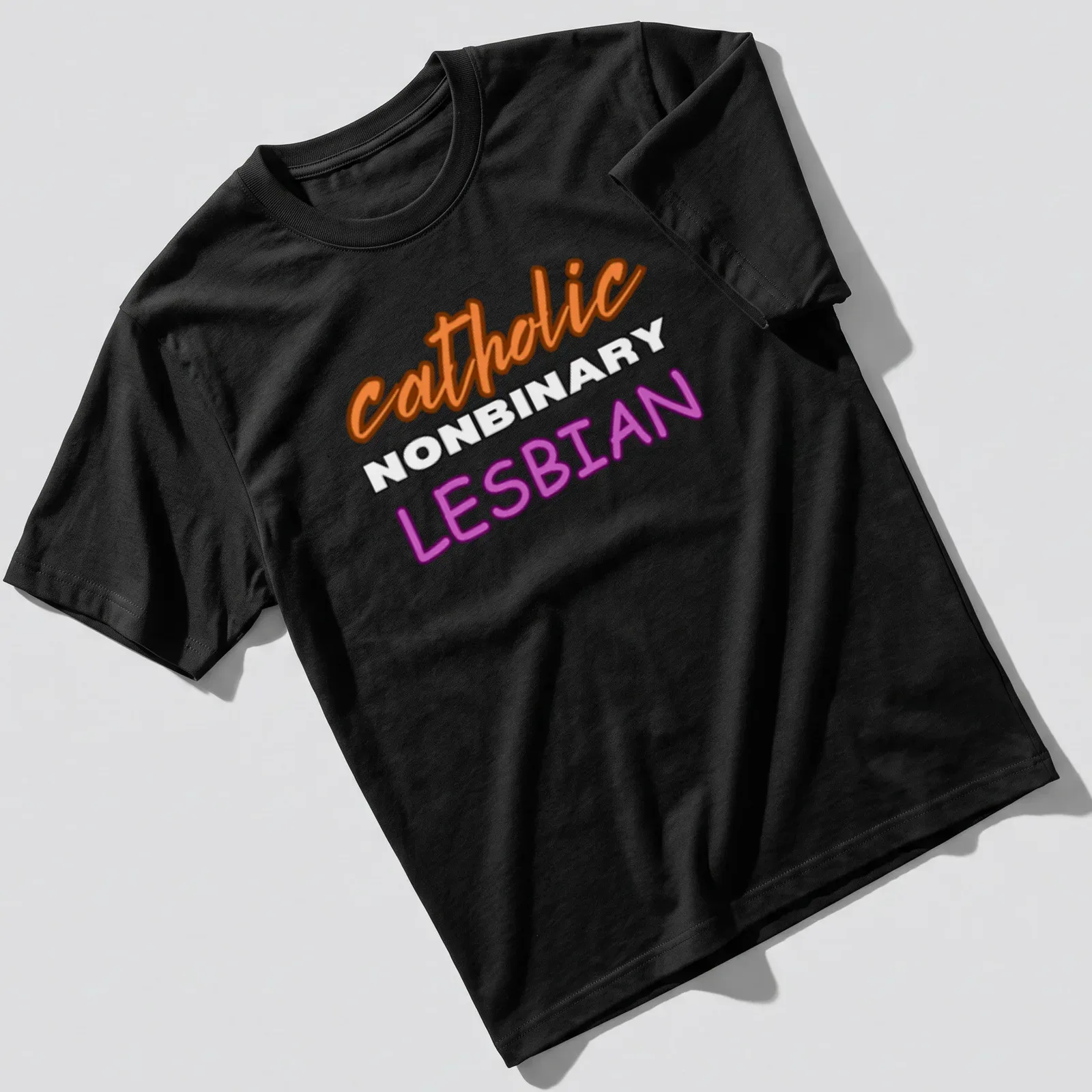 Bold typography design featuring 'catholic NONBINARY LESBIAN' in orange, white, and purple — printed on a unisex t-shirt