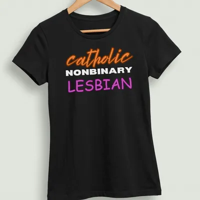 Bold typography design featuring 'catholic NONBINARY LESBIAN' in orange, white, and purple — printed on a women's shirt