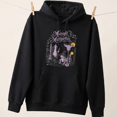 Whimsical illustration of a frog in a witch hat holding a margarita with candles around it — printed on a unisex hoodie