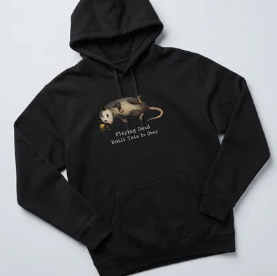 Realistic illustration of an opossum playing dead with humorous text — printed on a unisex hoodie