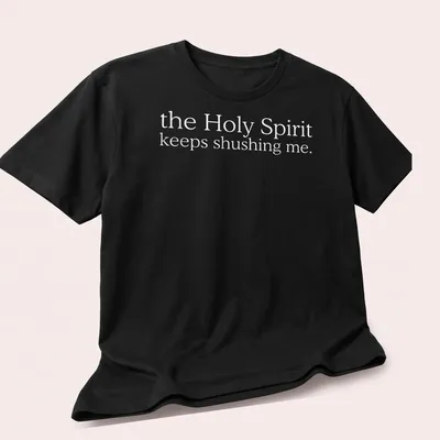 Simple white text reading 'the Holy Spirit keeps shushing me.' on a T-shirt. — printed on a unisex t-shirt (angled view)