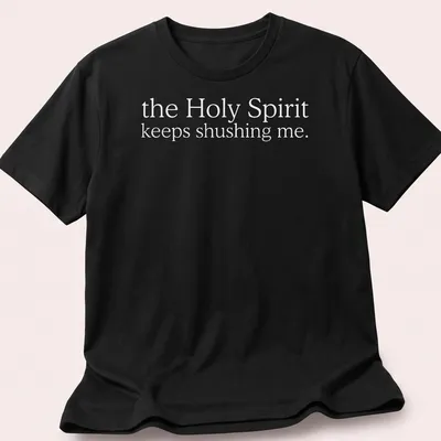 Simple white text reading 'the Holy Spirit keeps shushing me.' on a T-shirt.