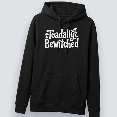 Cartoon toad graphic with playful text 'Toadally Bewitched' in green and black. — printed on a unisex hoodie